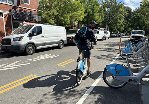 Person riding Divvy bike on street in contraflow lane past a Divvy bike docking station